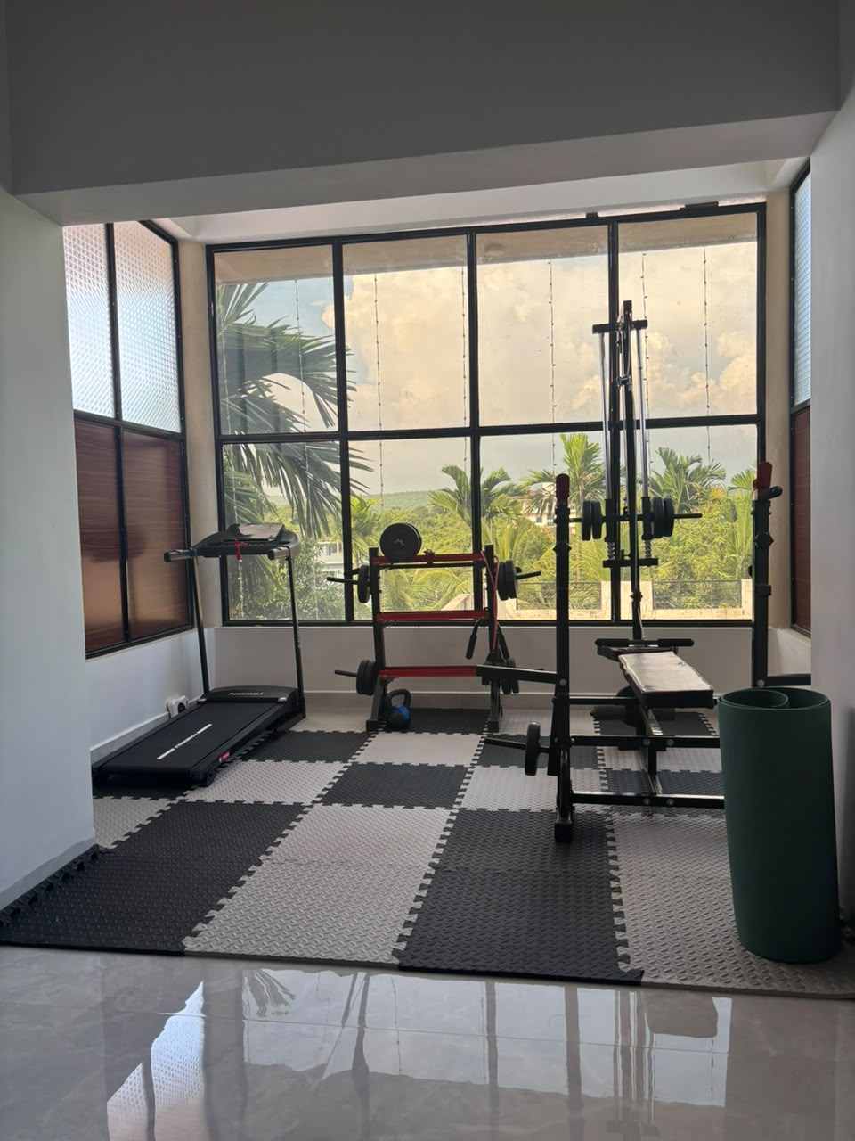 Gym at Mastani Goa with a weight bench, weight plates and a treadmill by large windows